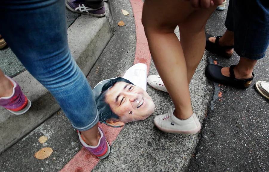Activists step over a picture of Shinzo Abe during a protest in front of the Japan Interchange Association in Taipei
